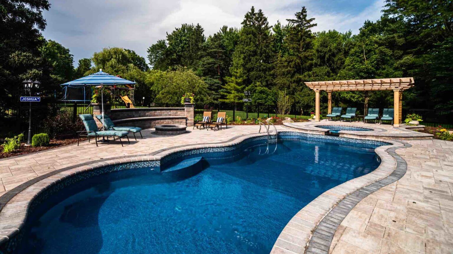 pool and hot tub with poolside firepit freeform pool builders se michigan fiberglass pool and spillover spa Custom inground pools Backyard pool ideas detroit Landscape se michigan Hardscape Clinton twp mi Patio designs Clinton twp mi