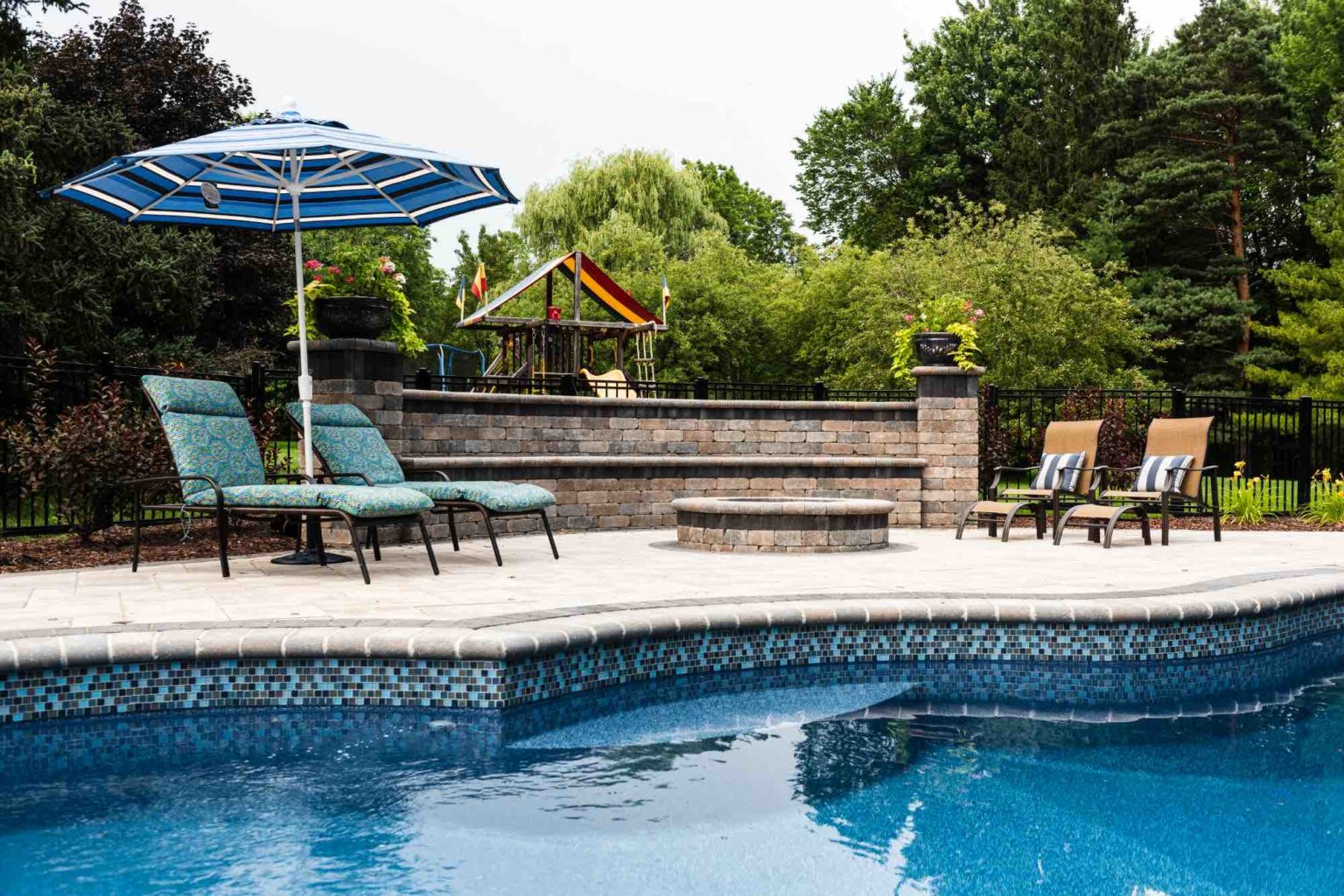 fire pit installed in poolside deck Custom inground pools Backyard pool ideas detroit
